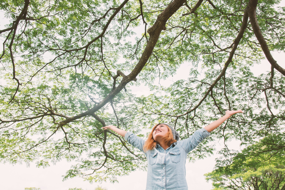 Femme heureuse levant les bras au milieu des arbres